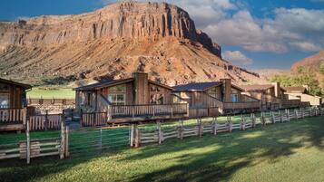 Un refugio rústico con cabañas de madera, un patio cercado y un paisaje montañoso de fondo.