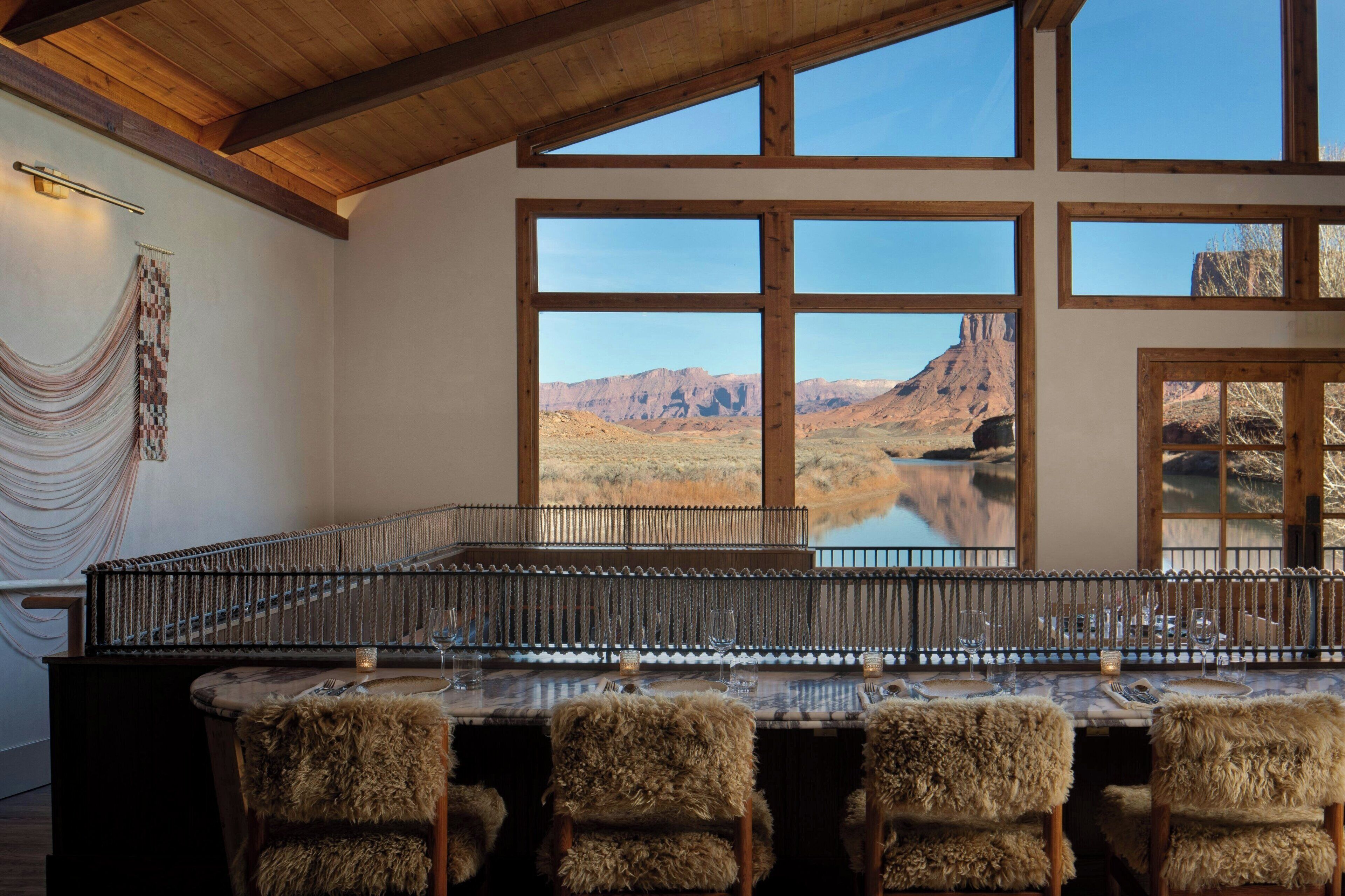 A dining area with a view of mountains and a lake, wooden beams on the ceiling, and a table set for four with chairs.
