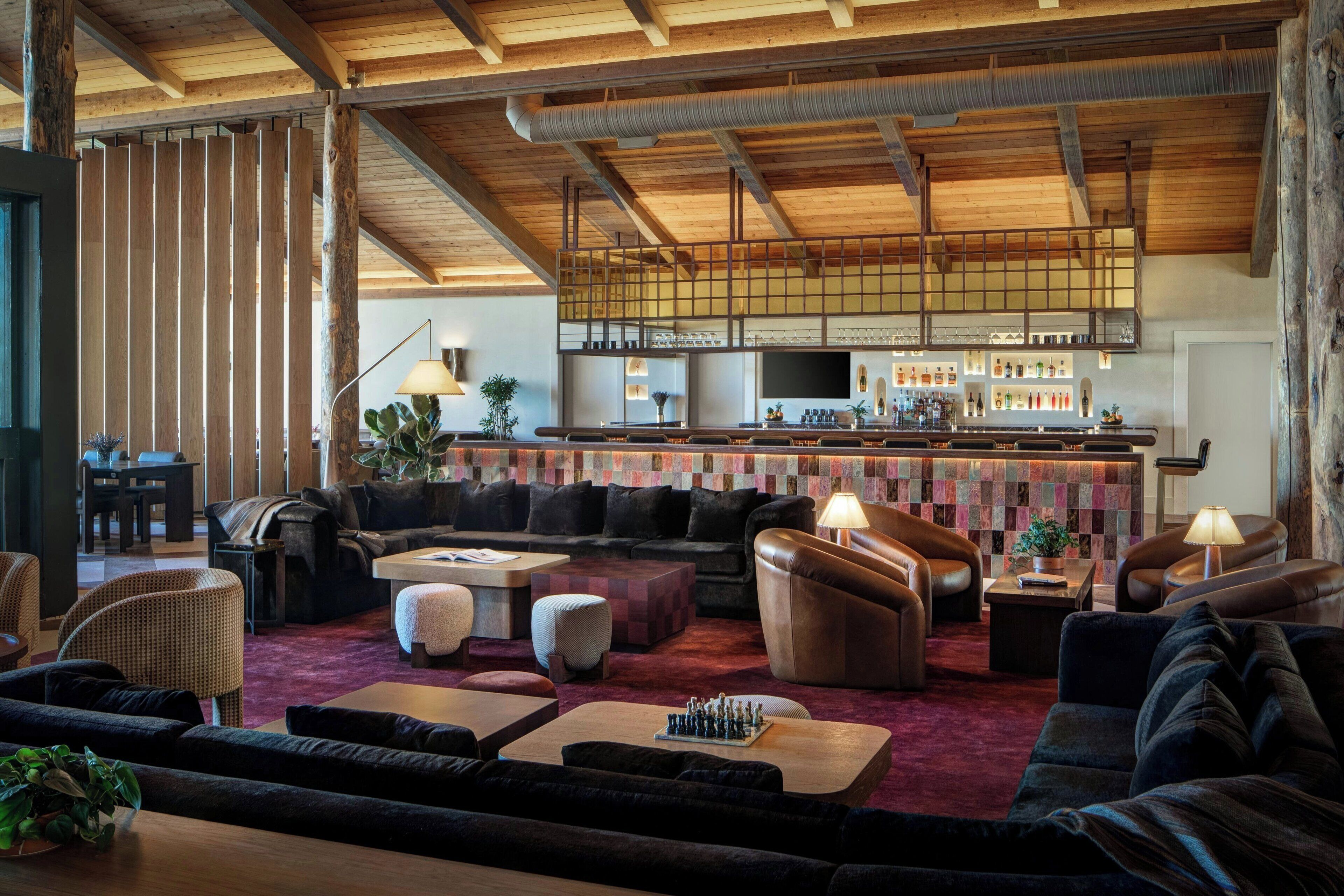 A spacious lounge area with multiple seating options, a bar with a variety of bottles, and a high ceiling with exposed beams.