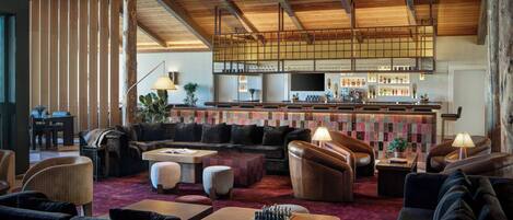 A spacious lounge area with multiple seating options, a bar with a variety of bottles, and a high ceiling with exposed beams.