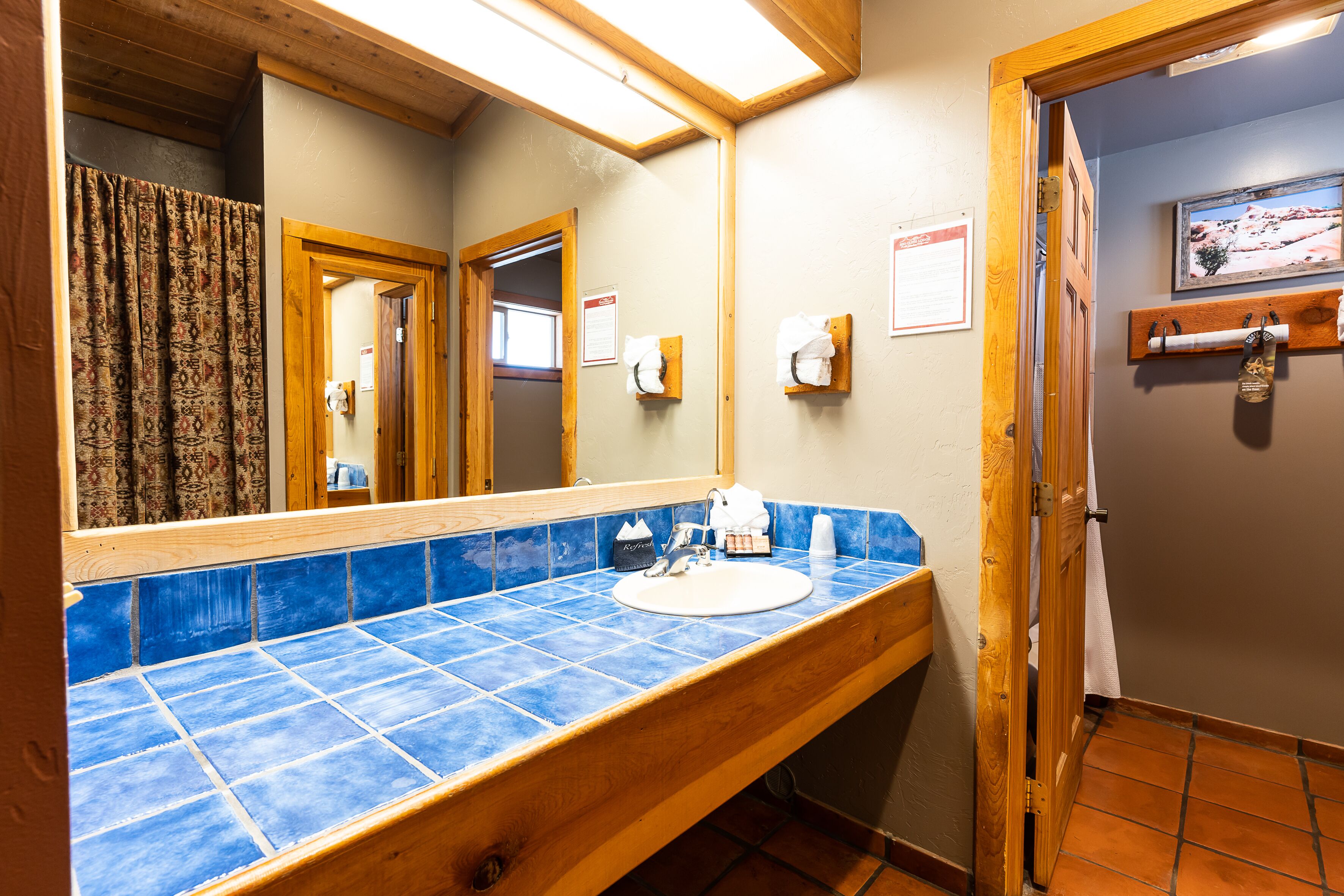 A bathroom with a blue-tiled sink, wooden vanity, and a mirror.