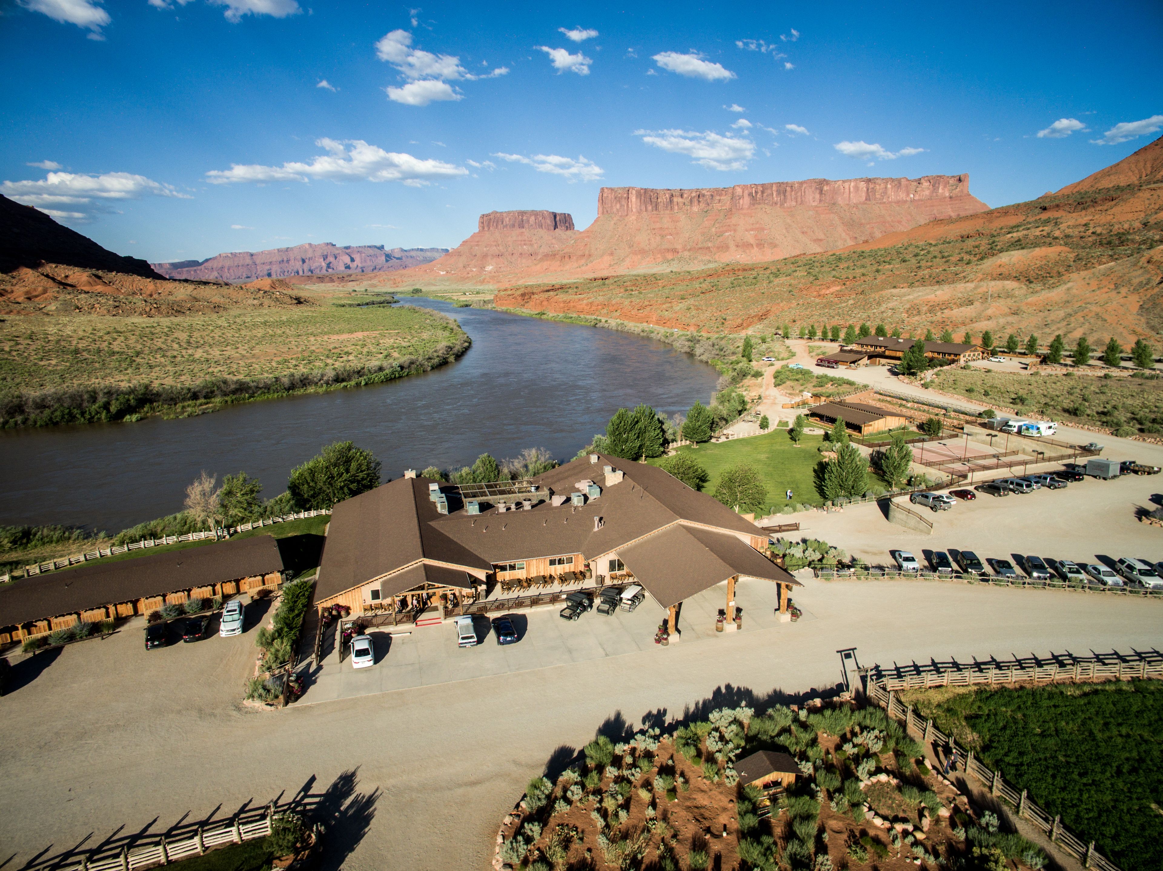 A hotel with a large parking lot, a river in the background, and a mountainous landscape.
