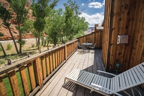 A wooden deck with a table and chairs, overlooking a river and mountains.
