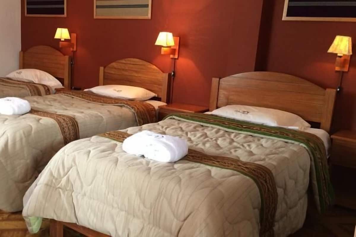 A hotel room with three single beds, each with a wooden headboard and a bedside lamp.