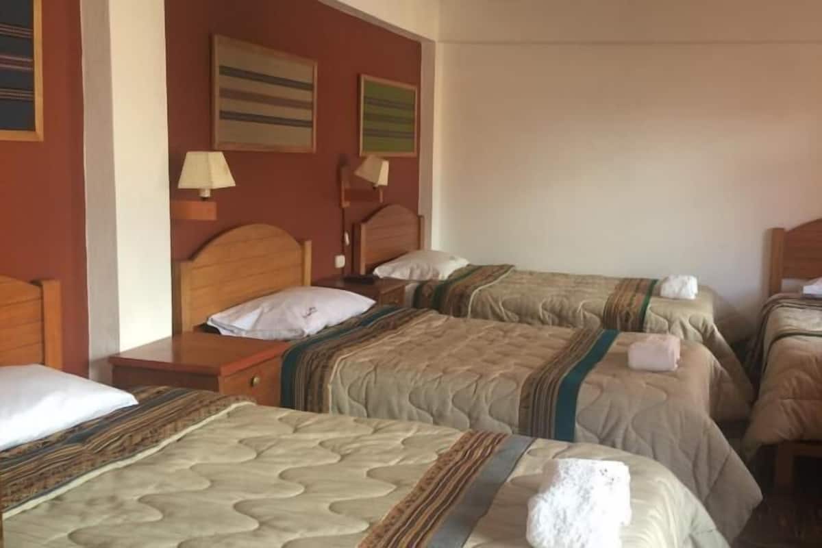 A hotel room with three single beds, wooden headboards, and a neutral color scheme.