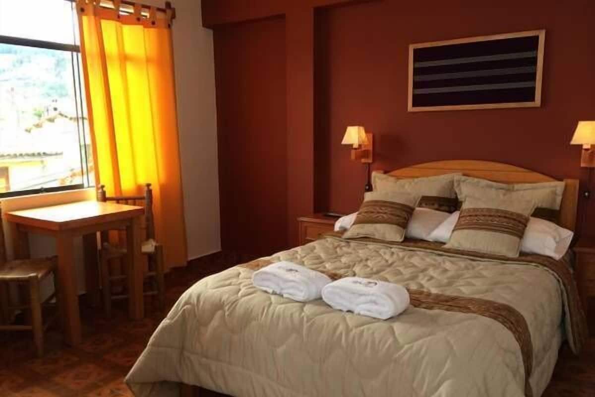 A neatly made bed with a quilted duvet, a wooden nightstand with a lamp, and a small table with chairs.