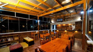 Un restaurante acogedor con mesas y bancos de madera, paredes de ladrillo y amplios ventanales con vistas a la ciudad de noche.