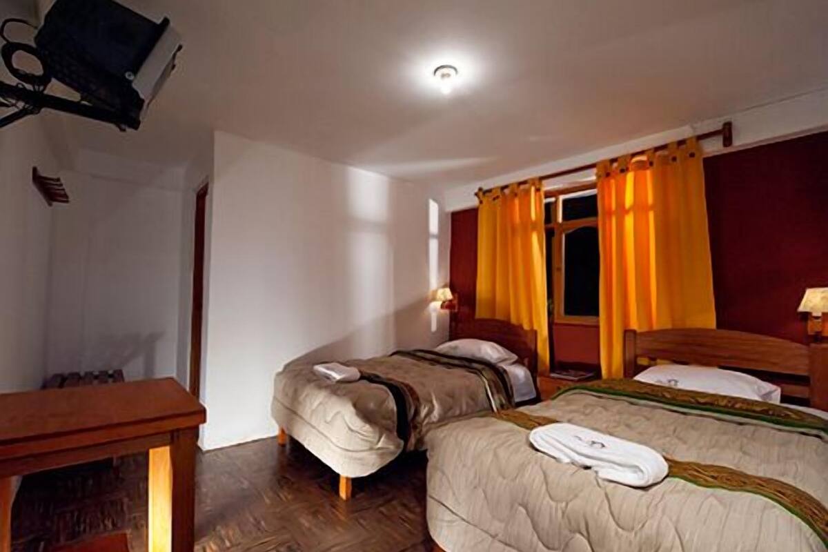 A hotel room with two beds, wooden flooring, a desk, and a television mounted on the wall.