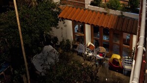 Un edificio de dos pisos con techo de tejas, un balcón y un patio con mobiliario exterior.