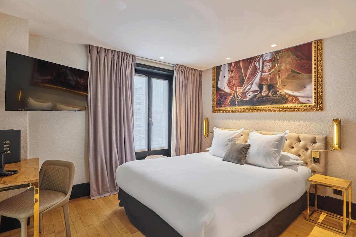 Habitación de hotel con una cama grande, un escritorio con silla, un televisor y un cuadro en la pared.