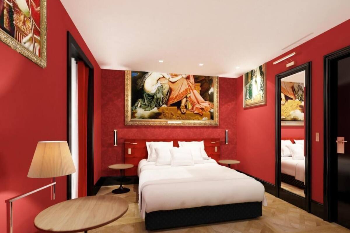 Habitación de hotel con una cama grande, una mesa redonda, una lámpara y un cuadro en la pared.