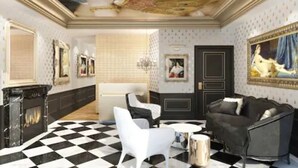 Una habitación con piso a cuadros, un sofá blanco y negro, un sillón blanco, una pequeña mesa redonda y una chimenea.