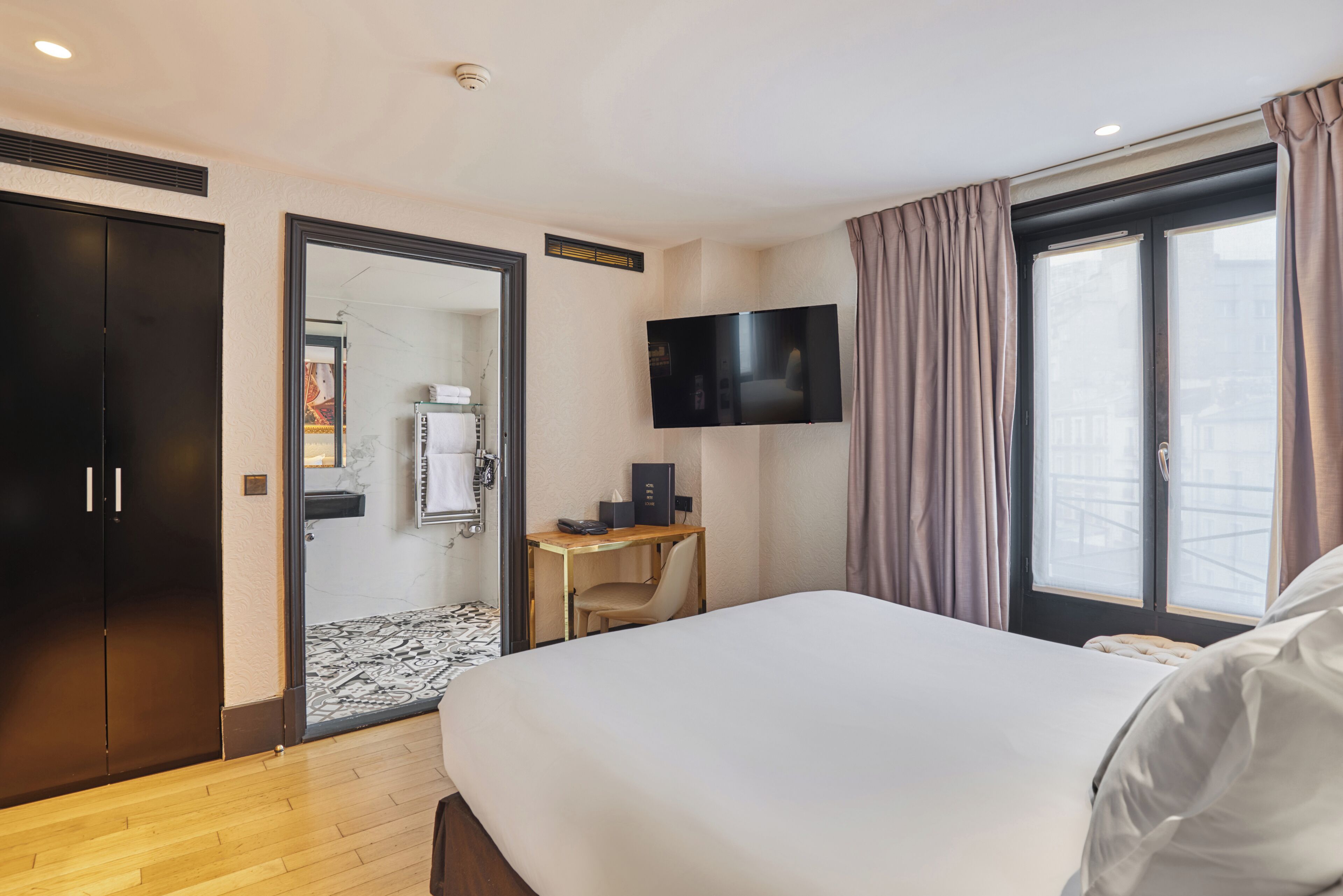 A hotel room with a large bed, a desk with a chair, a flat-screen TV, and a wardrobe.
