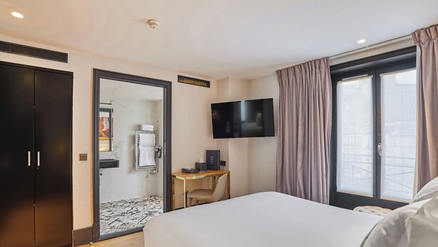 A hotel room with a large bed, a desk with a chair, a flat-screen TV, and a wardrobe. - Hôtel Eiffel Petit Louvre (Paris)