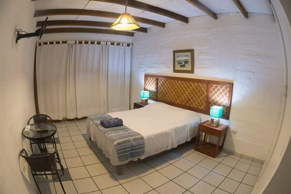 A bedroom with a bed, bedside lamps, a small table, and a chair.