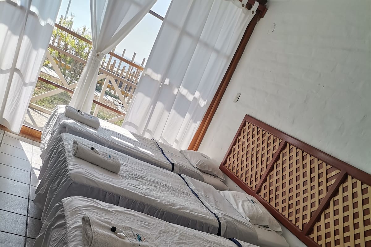 A row of neatly made beds with white linens and towels, a wooden lattice wall, and a tiled floor.