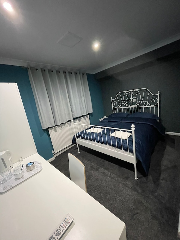 Um quarto com cama, escrivaninha, cadeira e radiador.