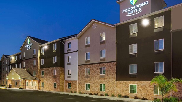 A multi-story hotel with a prominent 'Woodspring Suites' sign, featuring a modern architectural design with a mix of brick and stucco exteriors. - WoodSpring Suites Bakersfield East (Bakersfield)