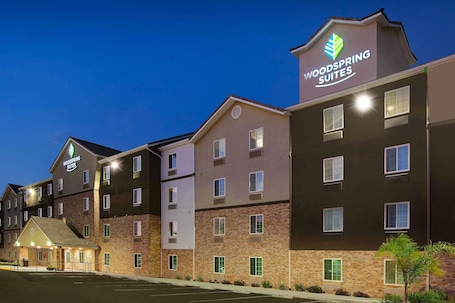A multi-story hotel with a prominent 'Woodspring Suites' sign, featuring a modern architectural design with a mix of brick and stucco exteriors.