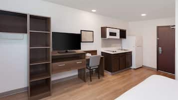 Una habitación moderna y compacta con cama, escritorio, silla, televisor, microondas y refrigerador.