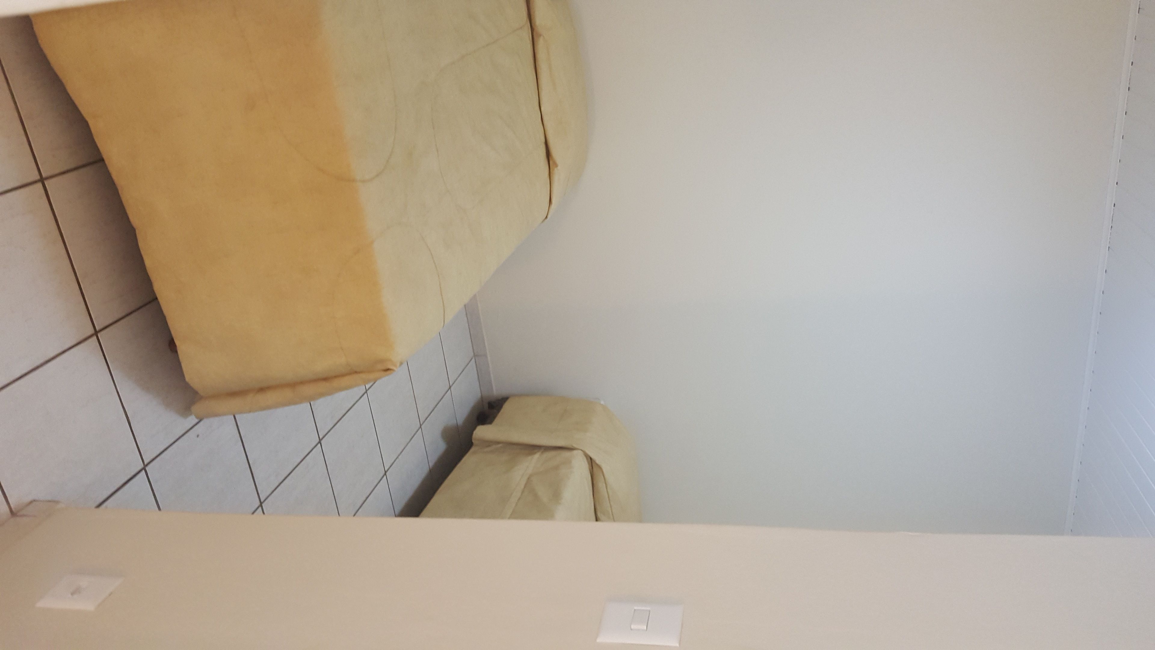 A corner of a room with a tiled floor, a white wall, and a beige curtain.
