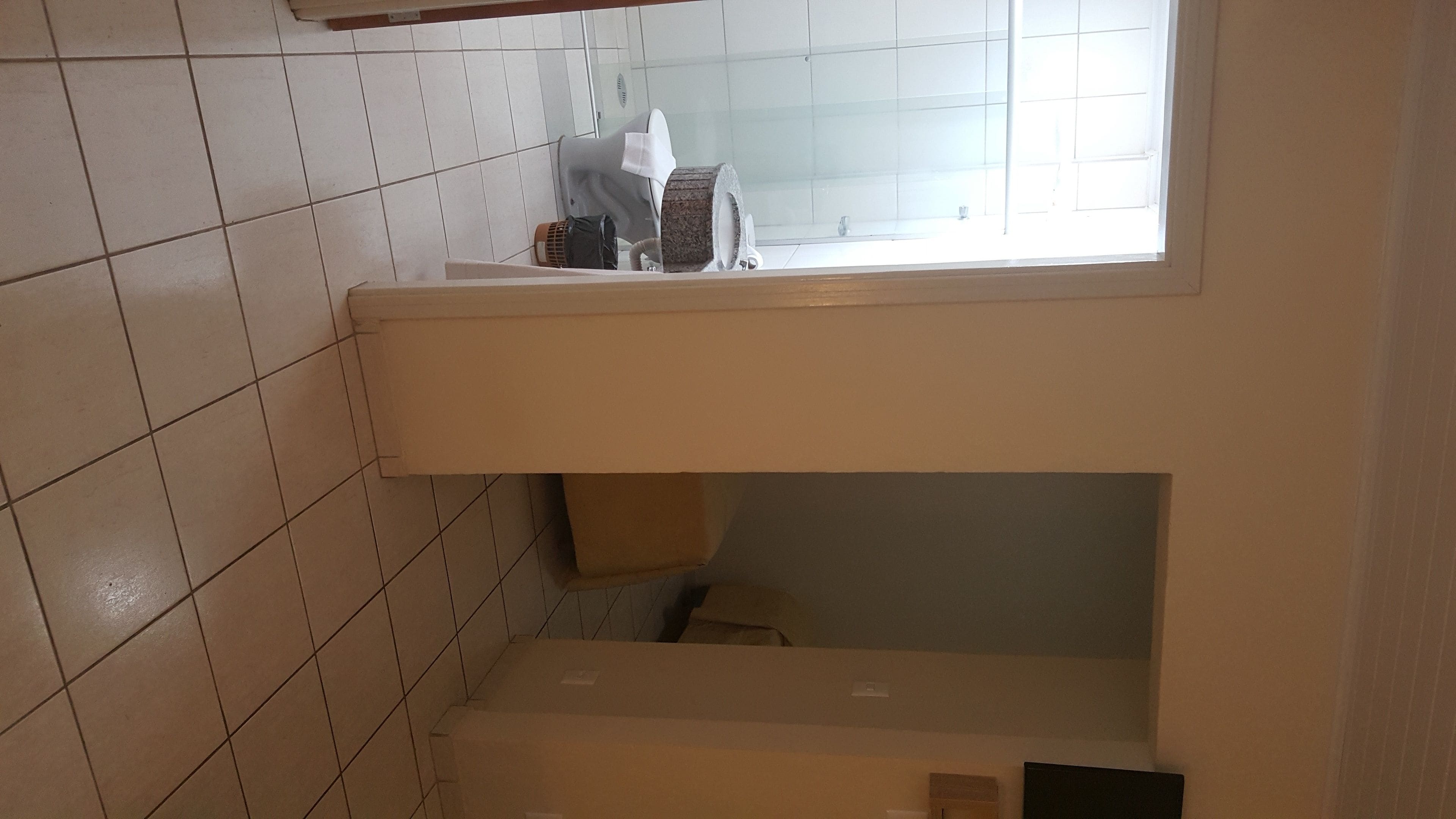 Un baño con paredes de azulejos blancos, una ventana y un estante con artículos de tocador.