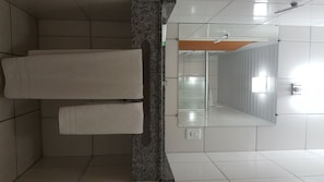 Une salle de bain avec deux serviettes blanches suspendues à un porte-serviettes, un comptoir en granit, un miroir et un sol carrelé.