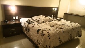 Habitación de hotel con una cama grande, una mesita de noche con teléfono y lámpara, y cabecero con iluminación integrada.