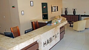Zona de recepción de un hotel con mostrador de mármol, sillas de madera y suelo de baldosas.