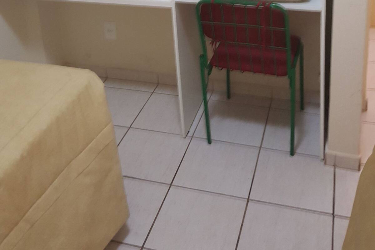 Une pièce comprenant un lit, une chaise, une étagère avec des couvertures pliées et un crochet fixé au mur.