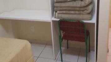 Una habitación con una cama, una silla, un estante con mantas dobladas y un gancho en la pared.