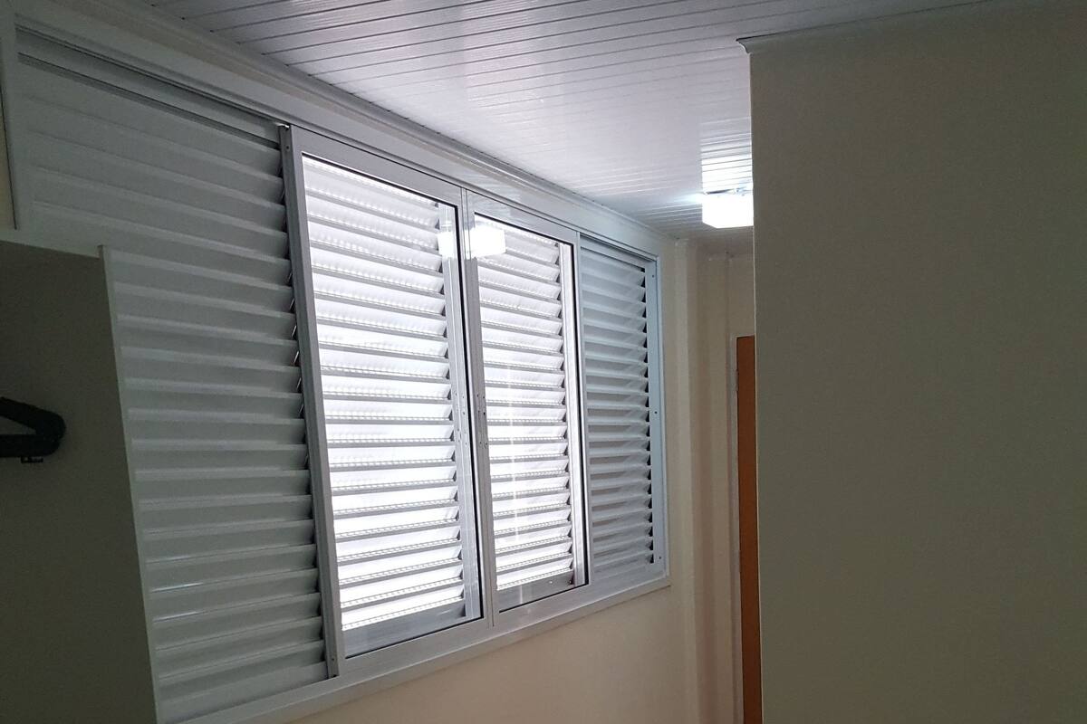 Une pièce avec un sol carrelé, un radiateur, une fenêtre avec des stores et un lit recouvert d’une couverture.