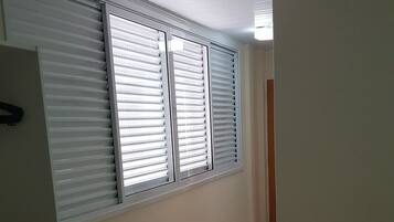 Una habitación con suelo de baldosas, un radiador, una ventana con persianas y una cama con una colcha.
