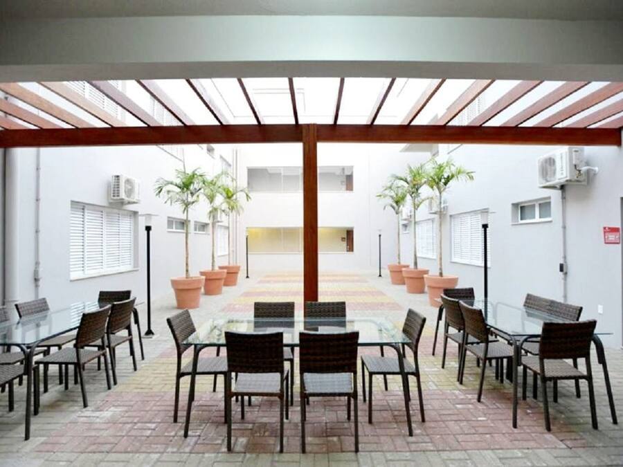 A conference room with a glass table and chairs, surrounded by potted plants and a wooden pergola.