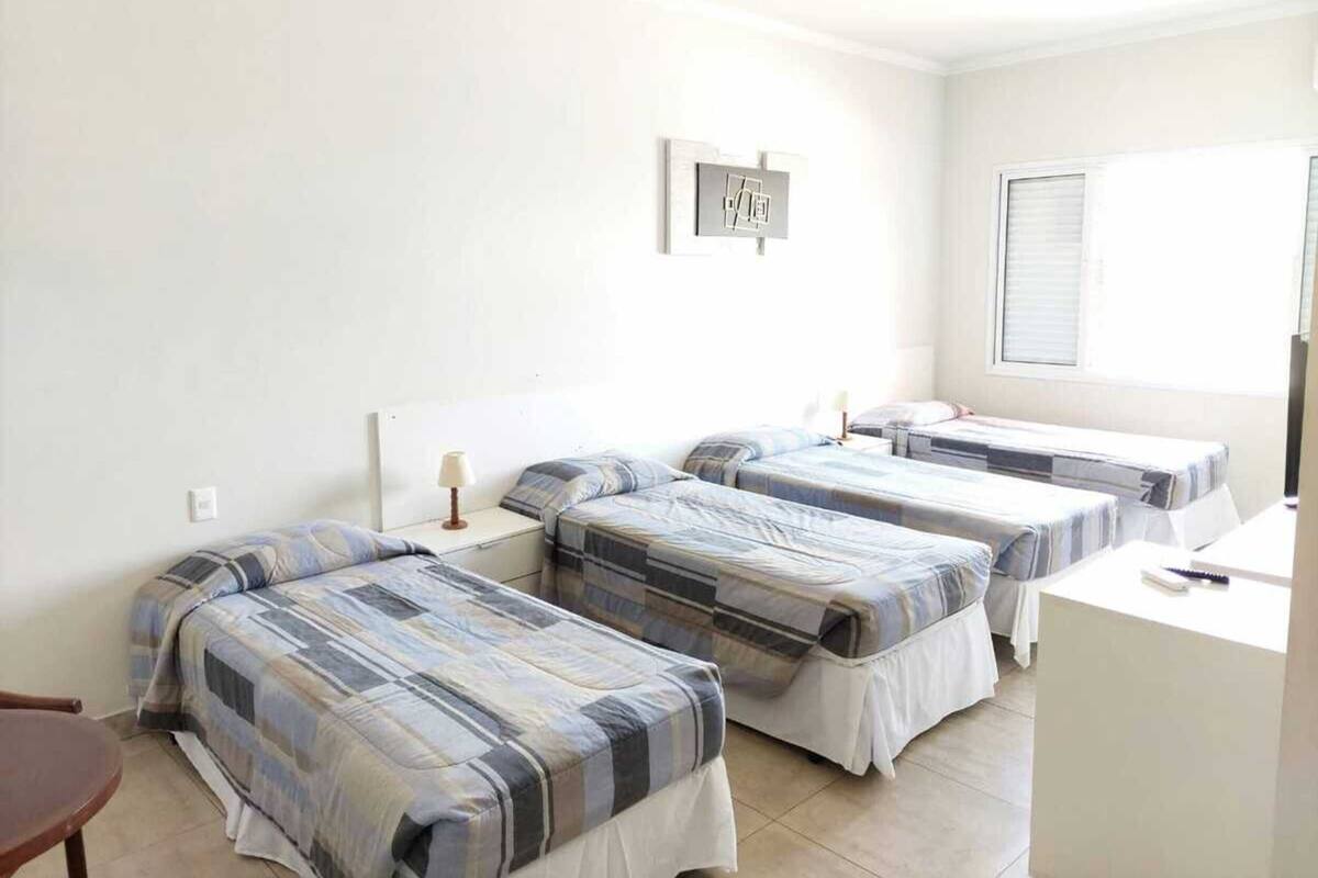 A hotel room with three single beds, a small desk, and a window with blinds.