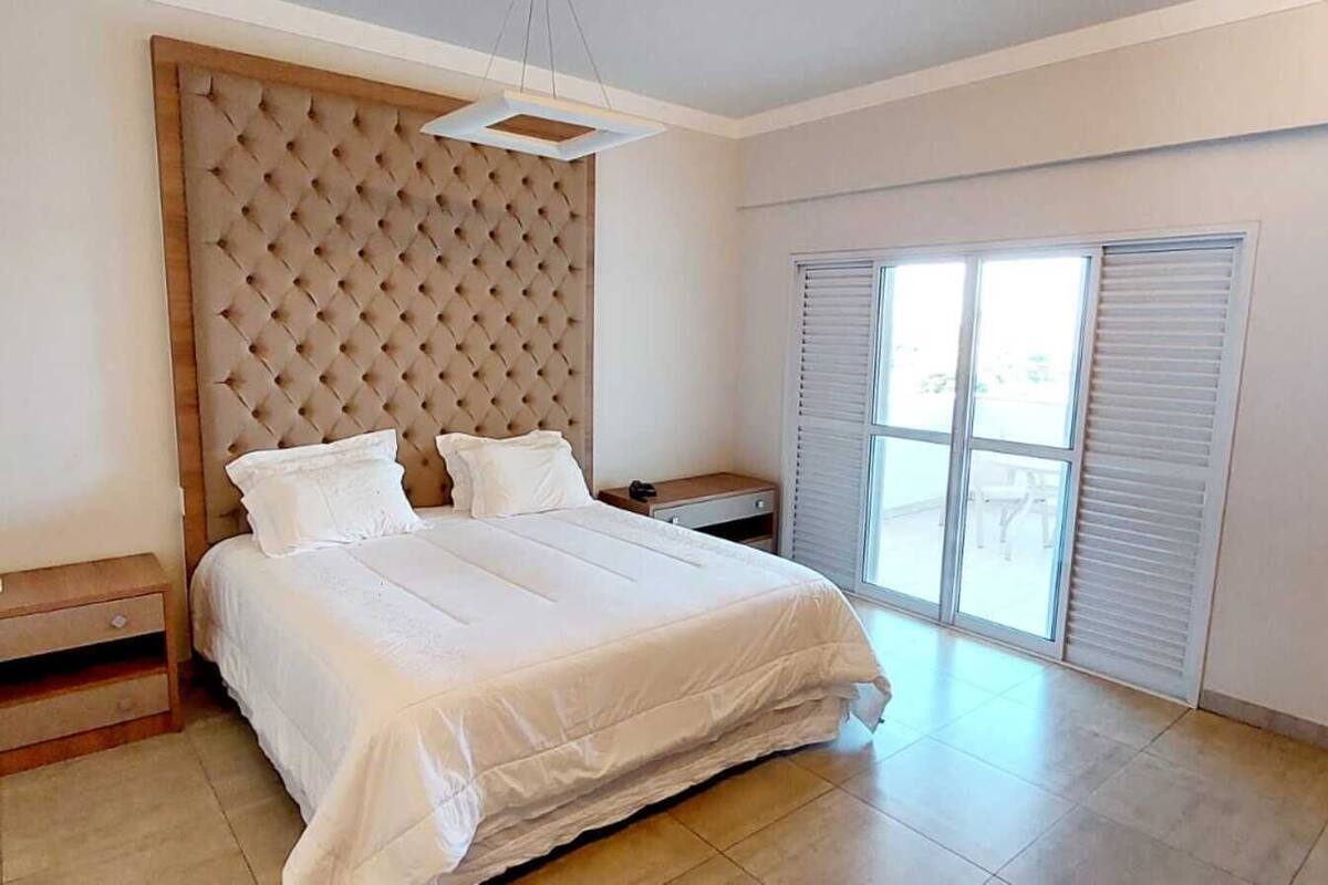 A bedroom with a large bed, a bedside table, a nightstand, and a window with blinds.