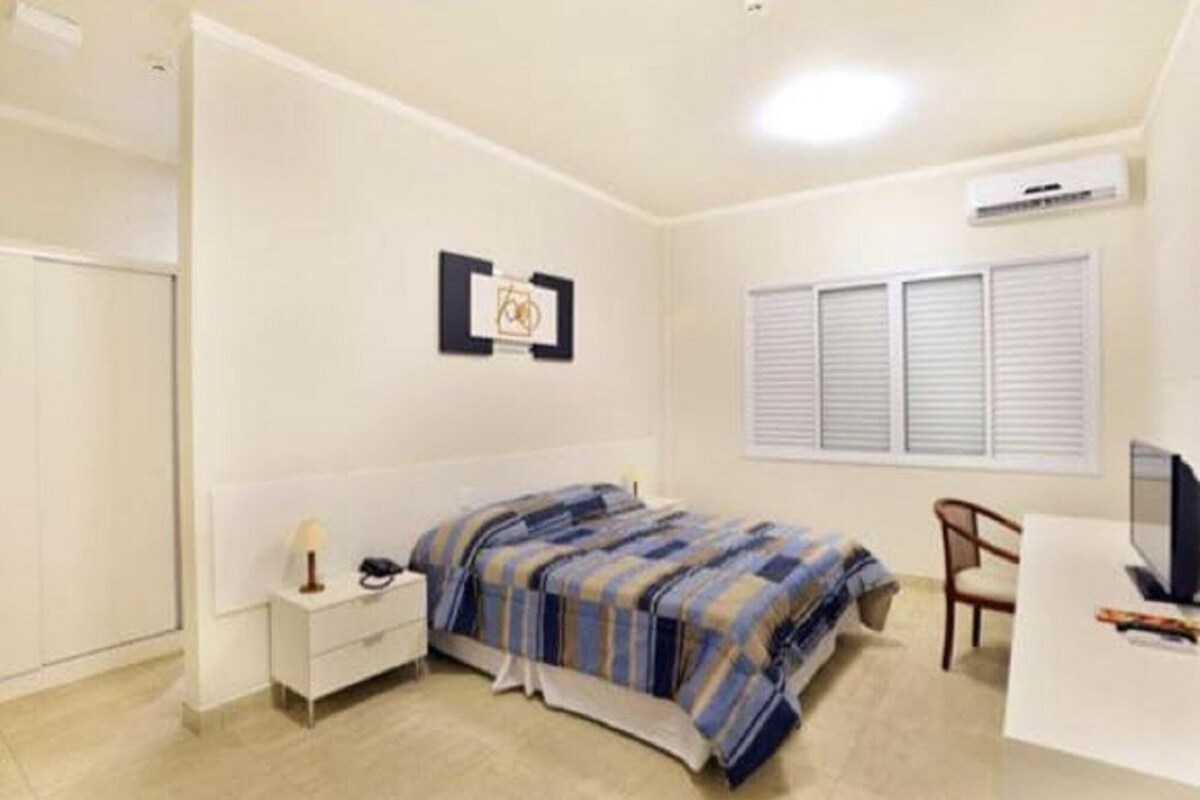A bedroom with a bed, bedside table, chair, and a desk with a computer.