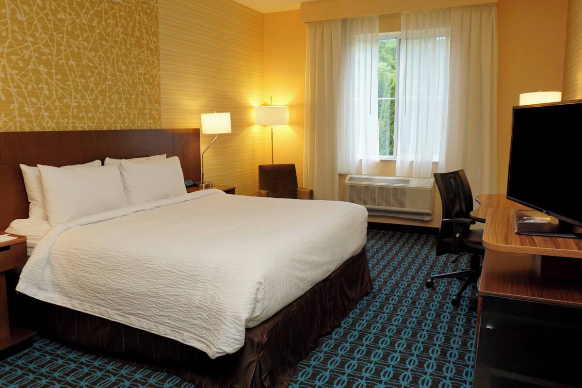 Une chambre d’hôtel avec un grand lit, deux lampes de chevet, un bureau avec un ordinateur, une télévision et une fenêtre avec des rideaux.
