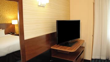 A hotel room with a bed, a television on a wooden stand, a nightstand, and a wall-mounted lamp.