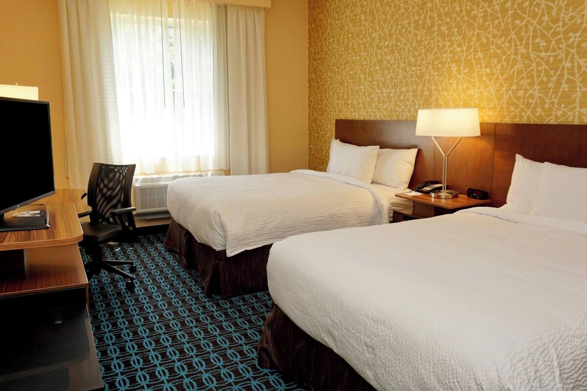 Une chambre d’hôtel avec deux lits, un bureau avec un ordinateur, une chaise et une fenêtre avec des rideaux.