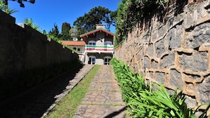 A stone pathway leading to a building with a red roof and a balcony. - Pousada Villaggio di Roma (Campos do Jordão)