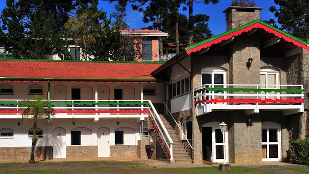 A two-story building with a red-tiled roof, white walls, and green and red trim. It features a balcony with white railings and a stone staircase leading to the upper floor. - Pousada Villaggio di Roma (Campos do Jordão)