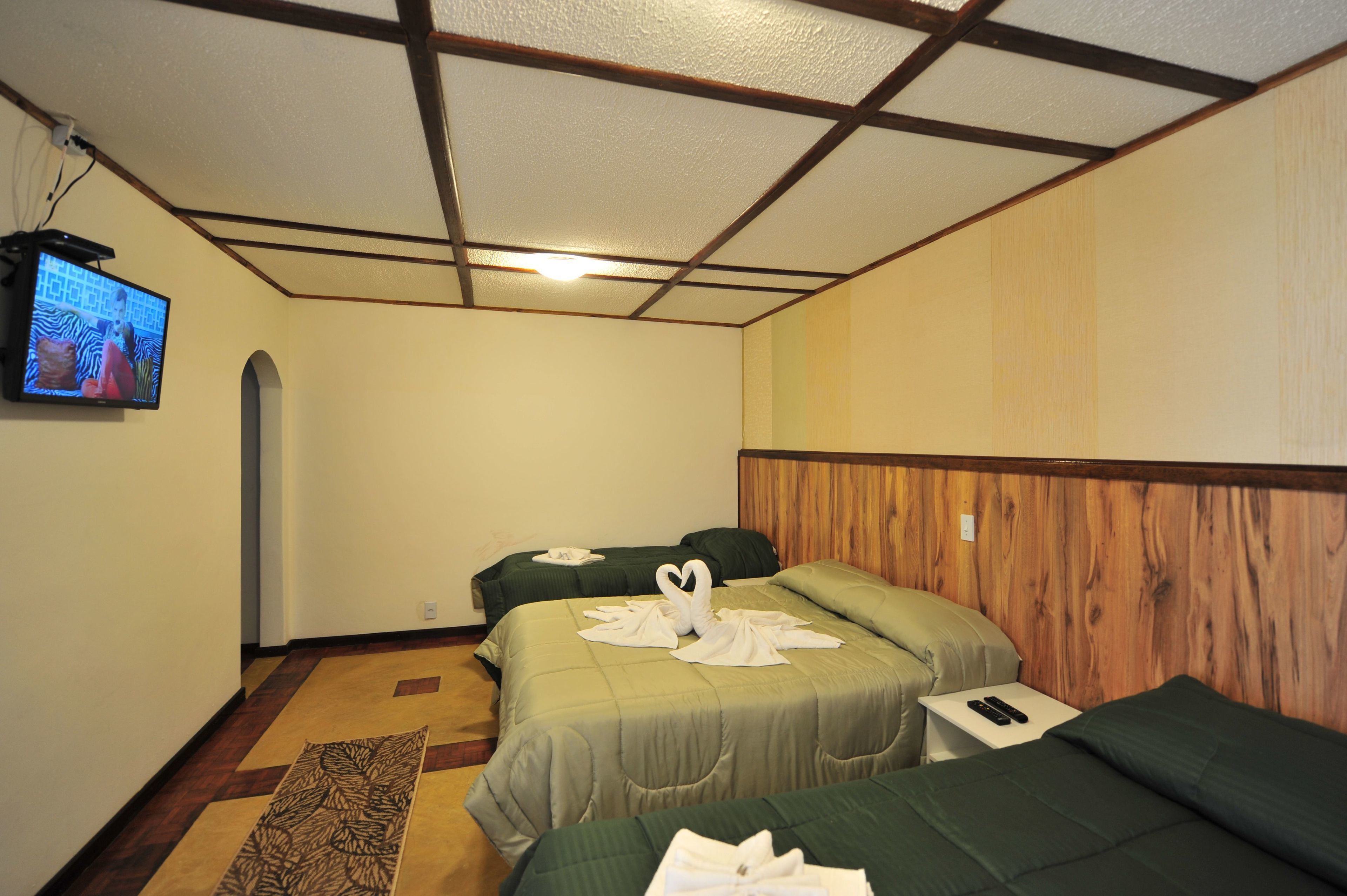 A hotel room with two beds, a television on the wall, and a wooden accent wall.