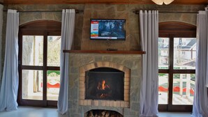 A fireplace with a TV above it, flanked by curtains and stone walls. - Pousada Villaggio di Roma (Campos do Jordão)