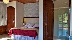 A bedroom with a bed, a wooden door, and a view of a garden through a glass door. - Pousada Villaggio di Roma (Campos do Jordão)