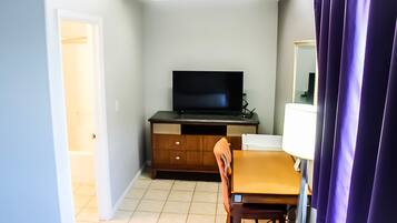 Una habitación pequeña con una televisión sobre un mueble de madera, una silla, una mesa y una cortina morada.