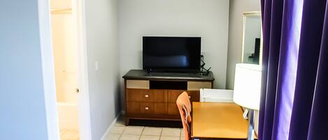 A small room with a television on a wooden cabinet, a chair, a table, and a purple curtain.