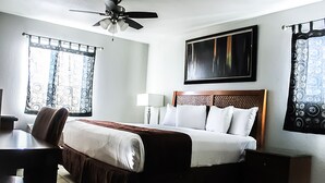 Une chambre d’hôtel équipée d’un lit, d’un bureau, d’une chaise, d’un ventilateur de plafond et de rideaux.