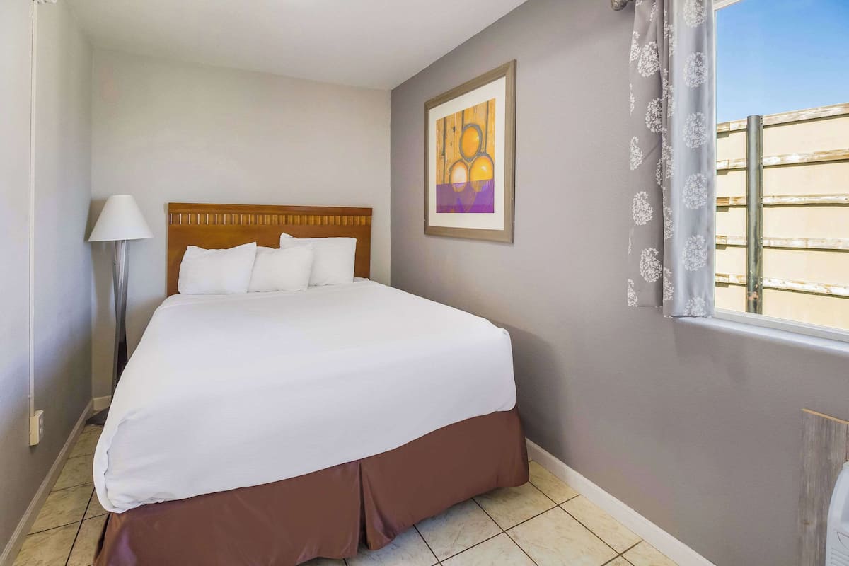 A neatly made bed with a wooden headboard, a floor lamp, and a framed artwork on the wall.