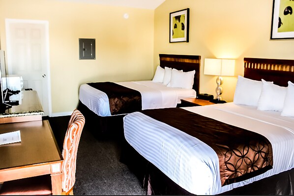 A hotel room with two beds, a desk, and a chair.